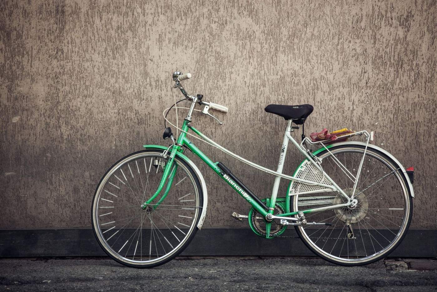 A green city bicycle leaning against a wall